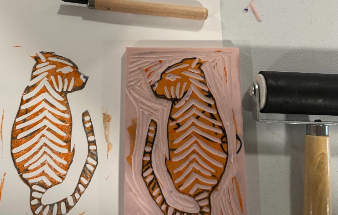 A lino-cut stamp of a tiger with a print and inking tool.